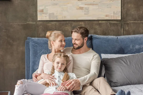 Feliz madre, padre e hija abrazando y sonriendo en casa - foto de stock