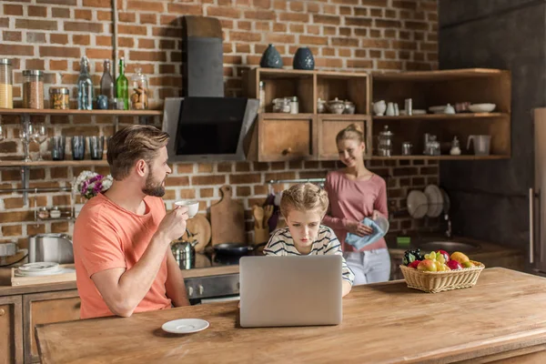 Menina bonito usando laptop com pais na cozinha — Fotografia de Stock