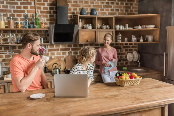 Linda niña usando el portátil con los padres en la cocina — Stock Photo