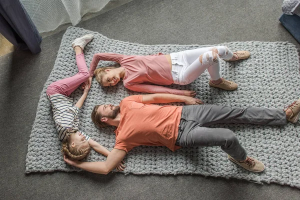 Vista de alto ângulo da família feliz deitada em conjunto no tapete de malha cinza — Fotografia de Stock