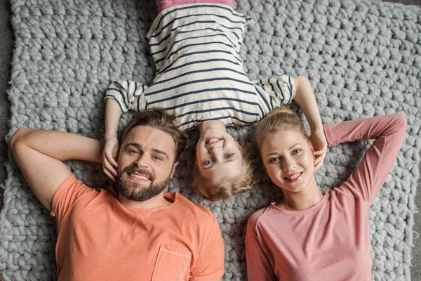 Draufsicht auf glückliche Familie mit einem Kind, das zusammen auf grauem Strickteppich liegt — Stockfoto