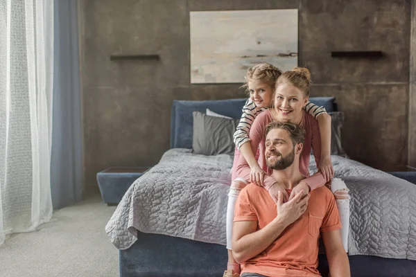 Счастливая молодая семья с одним ребенком, сидящая вместе и обнимающаяся в спальне — стоковое фото
