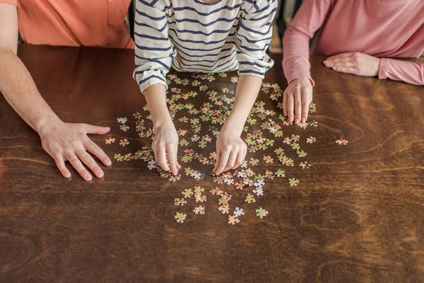 Vista parcial de cerca de la familia con un niño jugando con rompecabezas en la mesa - foto de stock