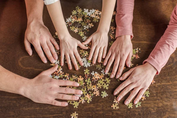 Close-up partial view of family with one child playing with puzzles on table — Stock Photo