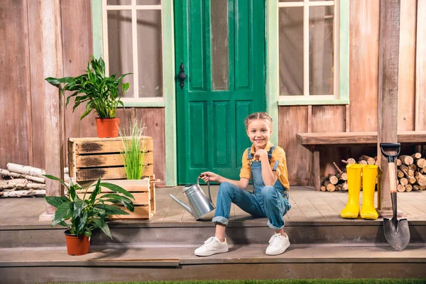 Entzückend lächelndes kleines Mädchen sitzt auf der Veranda mit Gießkanne — Stockfoto