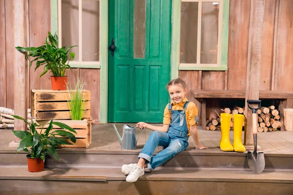 Adorable smiling little girl sitting on porch with watering can — Stock Photo