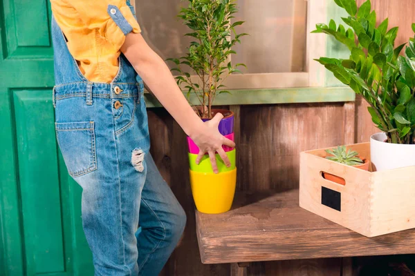 Close-up vista parcial da menina em dungarees segurando panelas coloridas no alpendre — Fotografia de Stock