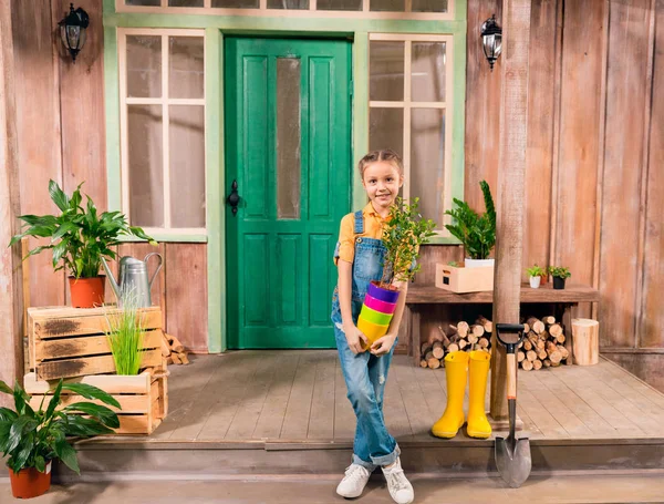 Adorável menina segurando vasos de flores coloridas com planta em casa e sorrindo para a câmera — Fotografia de Stock