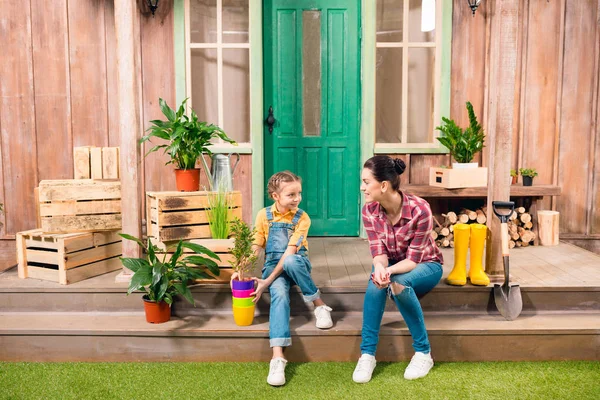 Felice madre e figlia con pianta in vaso seduti insieme sul portico e sorridenti l'un l'altro — Foto stock