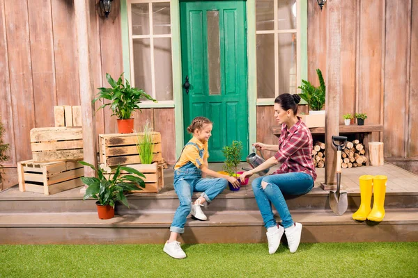 Happy mother and daughter sitting on porch and watering plant — Stock Photo