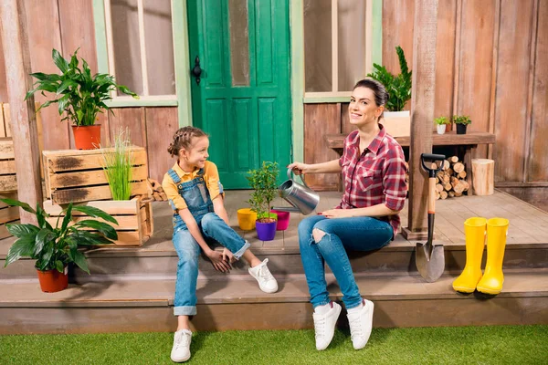 Happy mother and daughter sitting on porch and watering plant — Stock Photo