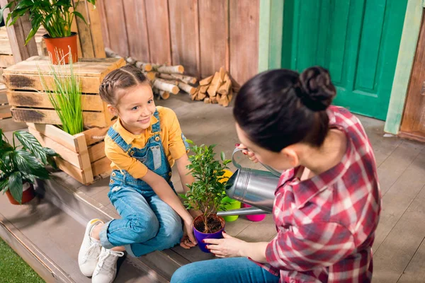 High angle view of mother and smiling daughter sitting on porch and watering plant — Stock Photo