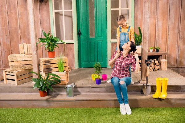 Mãe feliz e filha abraçando no alpendre com plantas em vasos — Fotografia de Stock