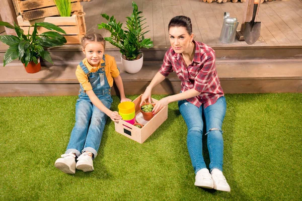High angle view of beautiful mother and daughter sitting on lawn with pots and potted plants — Stock Photo