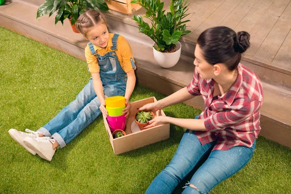 Vue grand angle de belle mère et fille assise sur la pelouse avec des pots et des plantes en pot — Photo de stock