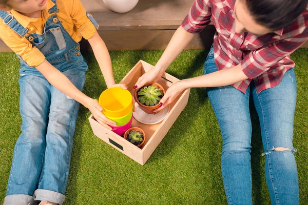 Close-up vista parcial de mãe e filha sentados no gramado com vasos e plantas em vaso — Fotografia de Stock