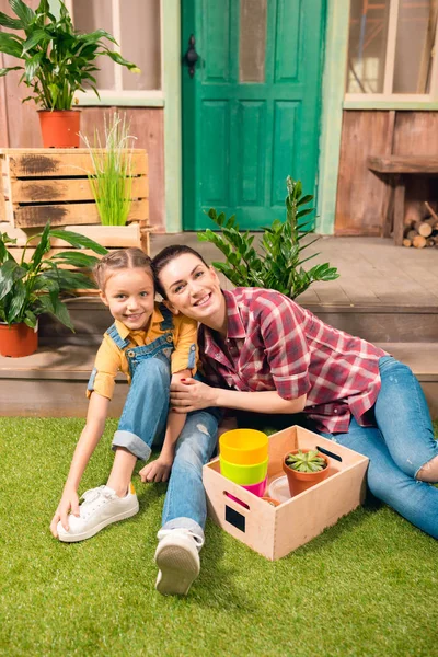 Happy mother and daughter sitting together on green lawn and smiling at camera — Stock Photo