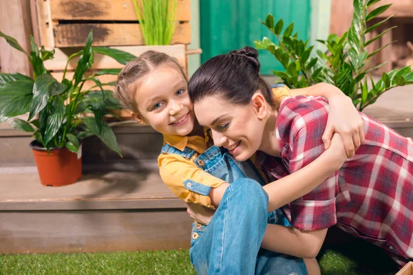 Glückliche Mutter und Tochter umarmen sich auf Veranda mit Topfpflanzen — Stockfoto