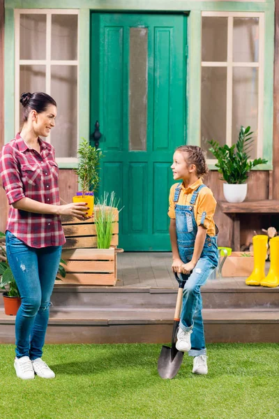 Mère souriante avec plante en pot et fille avec pelle de jardin se regardant — Photo de stock