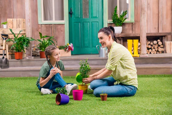 Mère et fille avec des plantes et des pots de fleurs assis sur l'herbe verte — Photo de stock