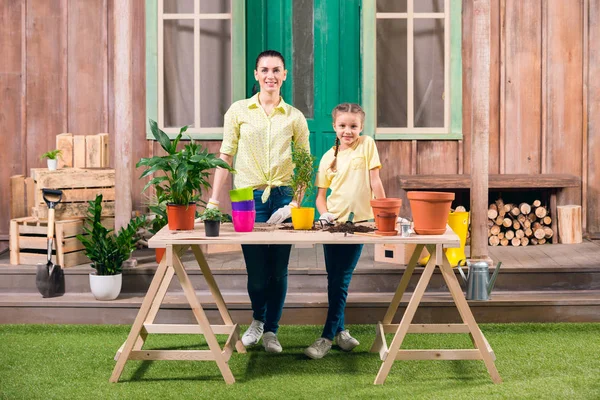 Madre e figlia con piante e vasi da fiori in piedi a tavola sul portico — Foto stock