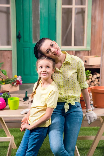 Madre e hija con plantas y macetas de pie y abrazos en la mesa en el porche - foto de stock