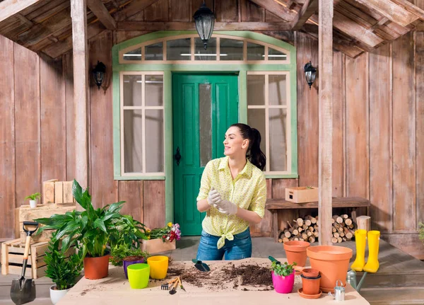 Mujer sonriente con plantas y macetas de pie en la mesa en el porche - foto de stock