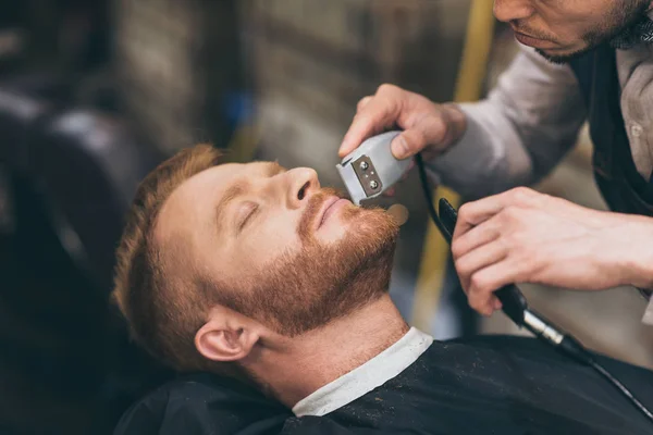 Barber trimming customers beard — Stock Photo