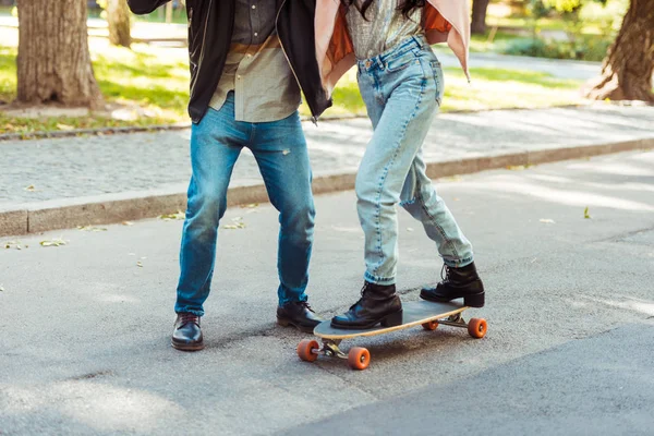 Petit ami aider petite amie patiner sur longboard — Photo de stock