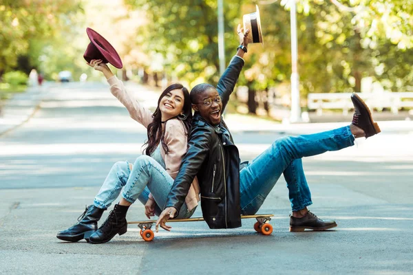 Couple sitting on longboard with hats in hands — Stock Photo