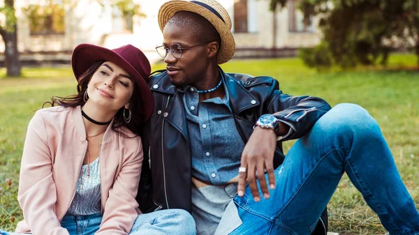 Pareja multicultural sentado en la hierba - foto de stock