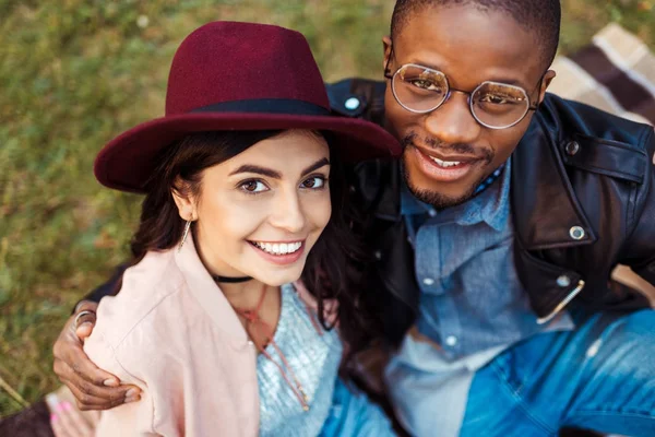 Pareja multicultural sentado en la hierba - foto de stock