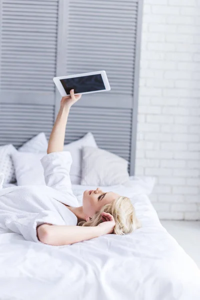 Молода жінка лежить на ліжку і використовує цифровий планшет з порожнім екраном — стокове фото