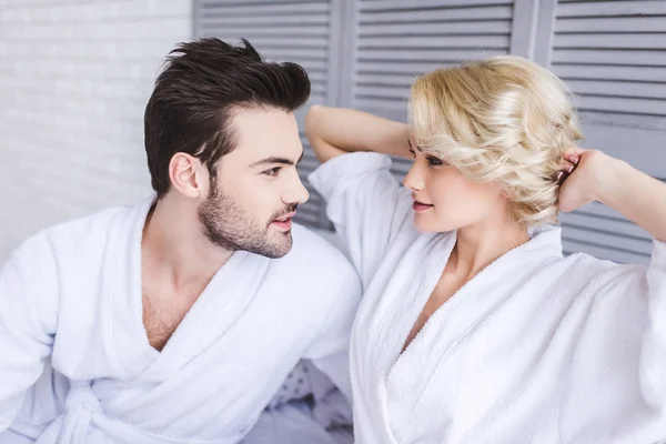 Beautiful young couple in bathrobes looking at each other in bedroom — Stock Photo