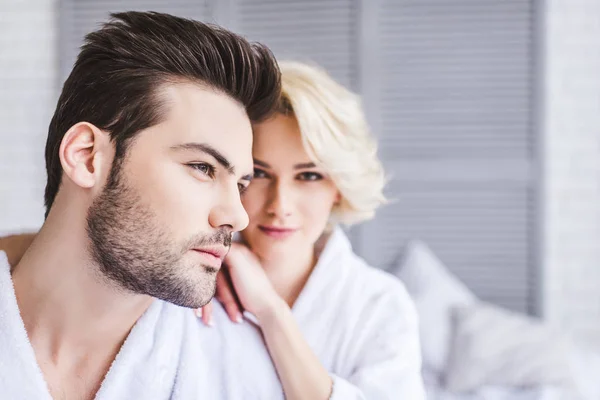 Beautiful young couple in bathrobes embracing on bed — Stock Photo