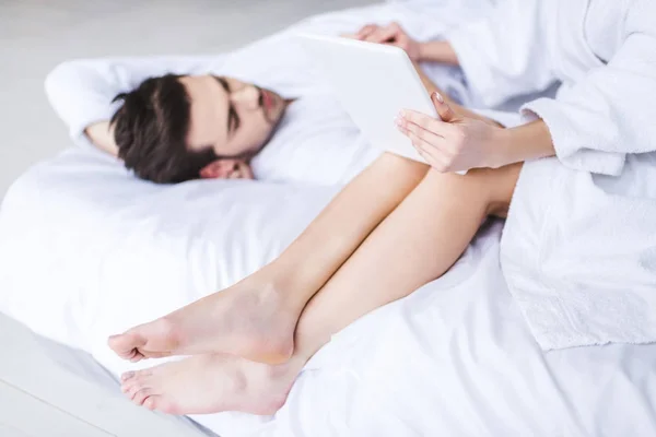 Cropped shot of girl using digital tablet while boyfriend lying on bed — Stock Photo