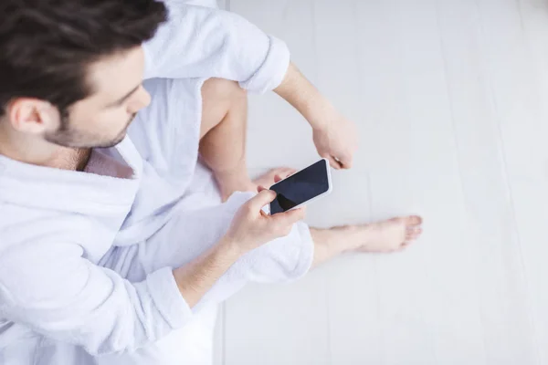 Schnappschuss eines bärtigen Mannes im Bademantel mit Smartphone mit leerem Bildschirm — Stockfoto