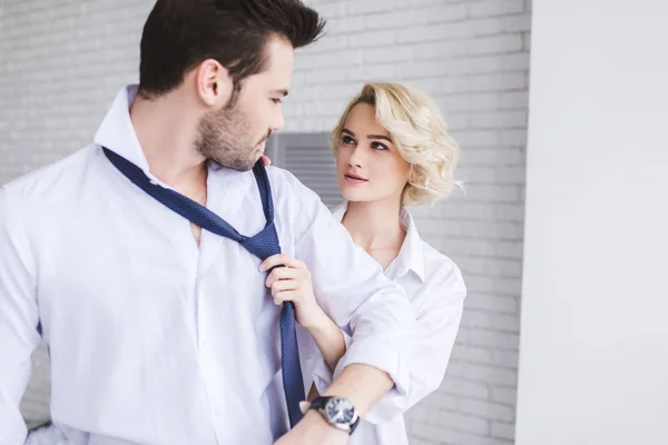 Joven pareja mirándose mientras mujer sosteniendo corbata de guapo novio - foto de stock