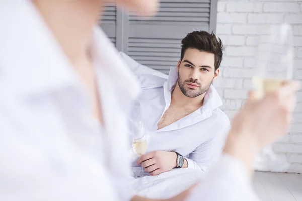 Selective focus of handsome man looking at girlfriend drinking champagne in bedroom — Stock Photo