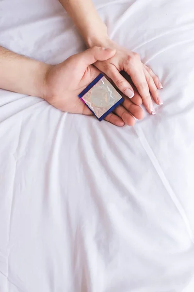 Обрезанный снимок молодой пары, держащей презерватив на кровати — стоковое фото