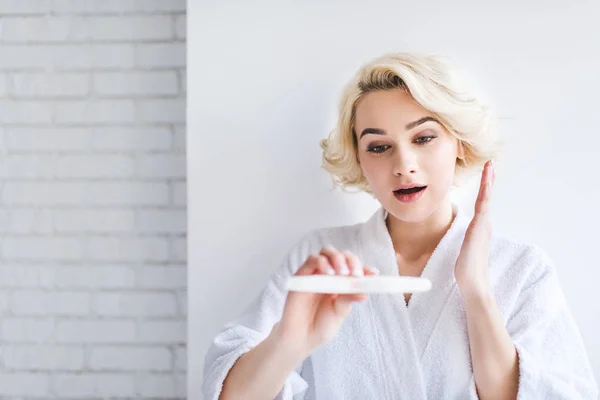 Surprised young woman in bathrobe holding pregnancy test — Stock Photo