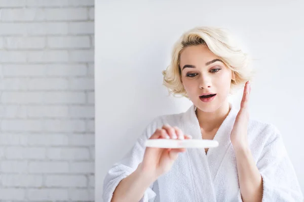 Überraschte junge Frau im Bademantel mit Schwangerschaftstest — Stockfoto