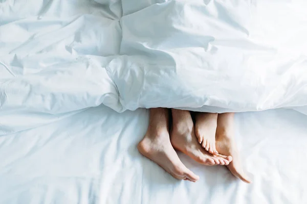 Cropped image of boyfriend and girlfriend lying in bed under blanket — Stock Photo