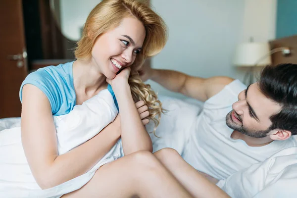Sonriente pareja mirándose en la cama por la mañana - foto de stock