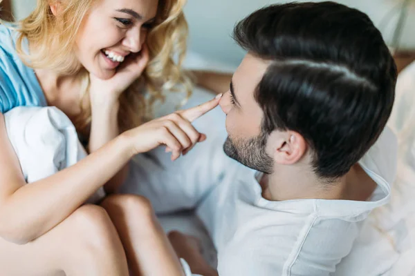 Sonriente novia tocando novio nariz en cama por la mañana - foto de stock