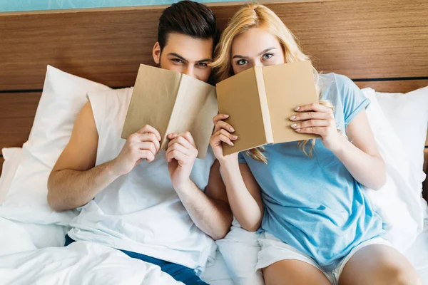 Sonriente pareja mirando hacia fuera de libros en la cama - foto de stock