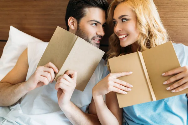 Couple souriant avec des livres au lit se regardant — Photo de stock