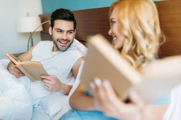 Sorrindo namorado e namorada com livros na cama olhando um para o outro — Fotografia de Stock