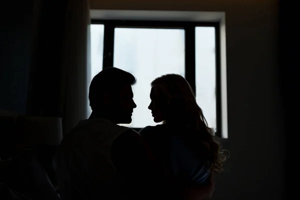 Силуэты гетеросексуальной пары, смотрящей друг на друга в темной комнате — стоковое фото
