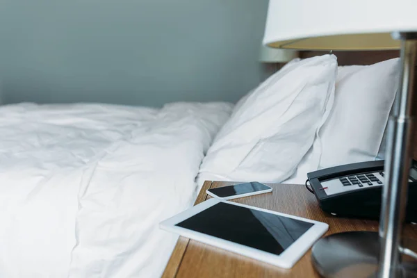 Smartphone y tableta en la mesita de noche en la habitación del hotel - foto de stock